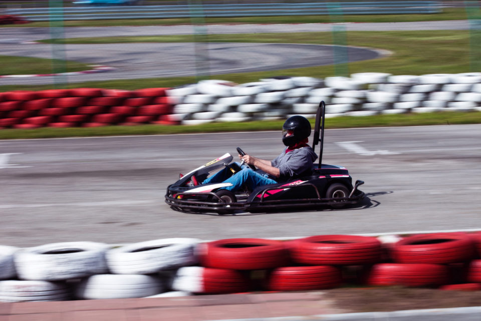 A Man in a go cart zooming on a race track with red and white tires as guard rails. - Best Birthday parties around Katy