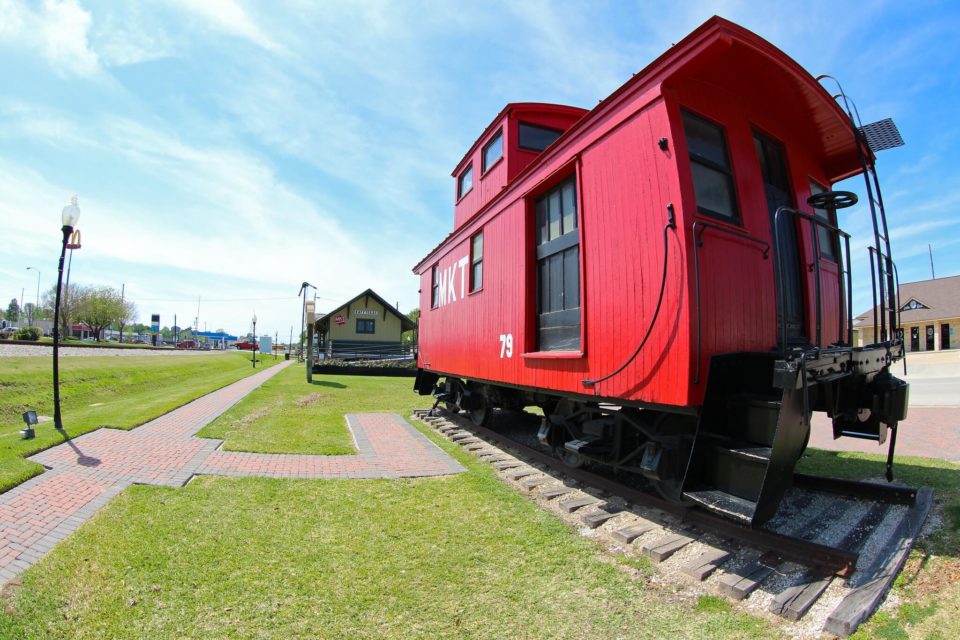Red cololers MKT railways caboose with MKT building in the background. Things to do with kids in Katy TX